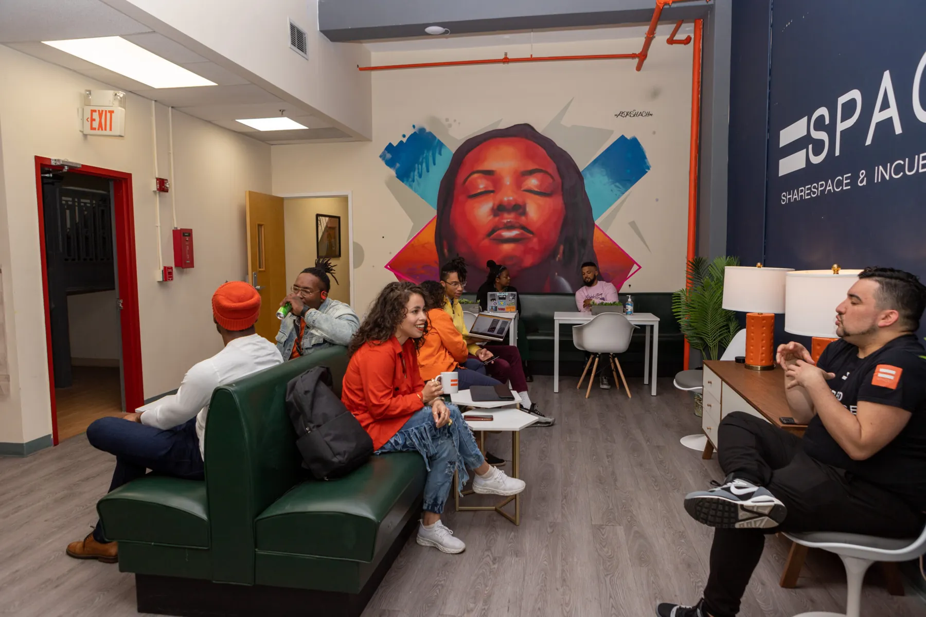Members talking on green leather booths beneath a large painted mural at EqualSpace's ES89 campus in Newark