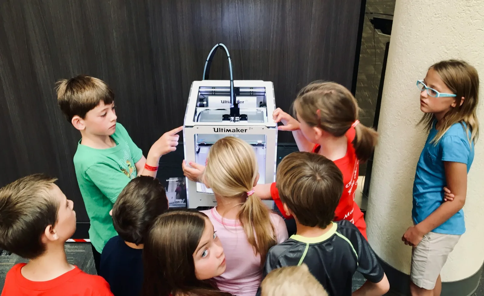 Children gathered around a 3D printer during an after-school STEAM session