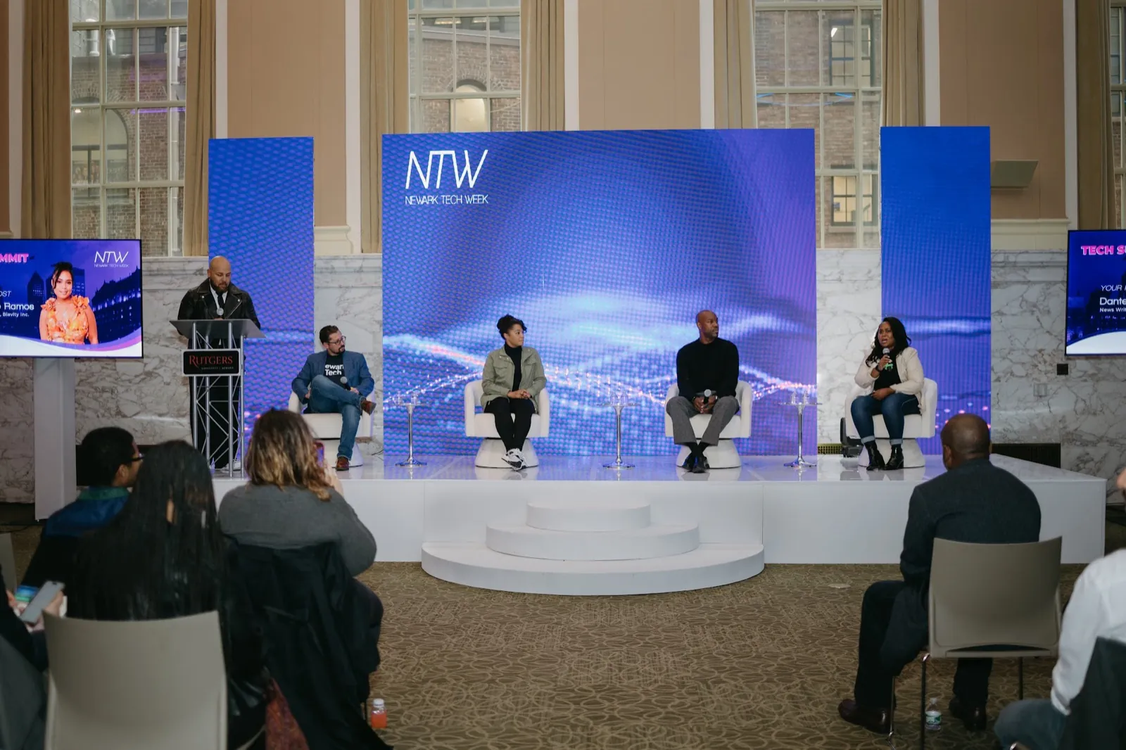 Panel discussion on a lit stage in front of a Newark Tech Week backdrop
