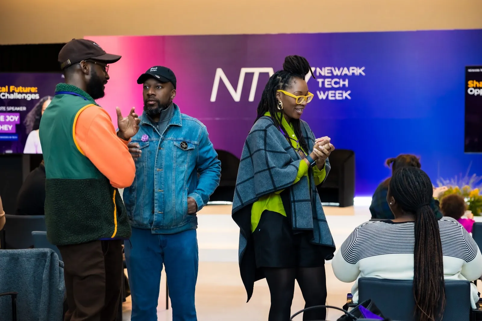 Attendees in conversation in front of a glowing Newark Tech Week sign